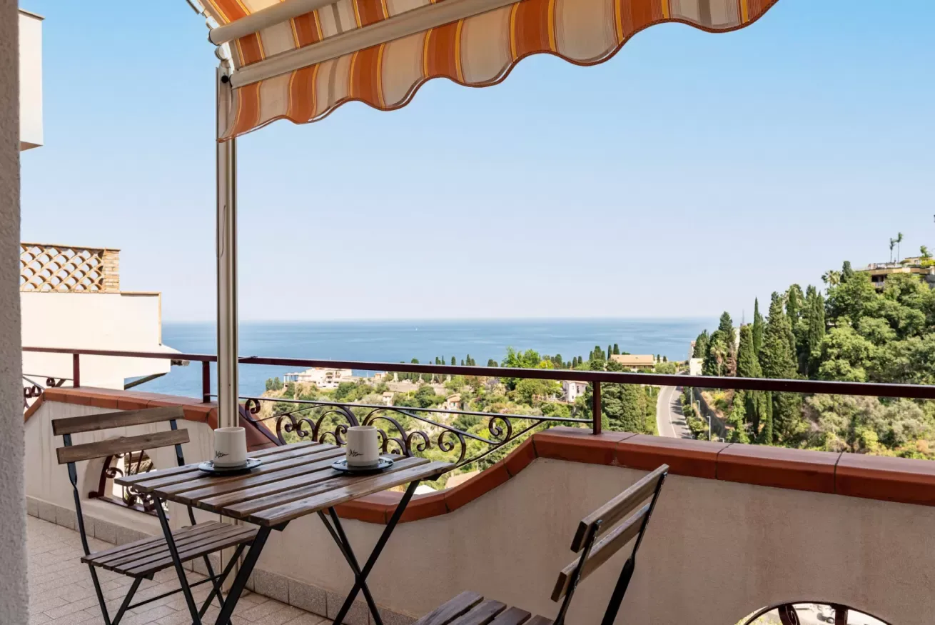 Una zona de comedor en un balcón tiene vistas al mar bajo un toldo a rayas.