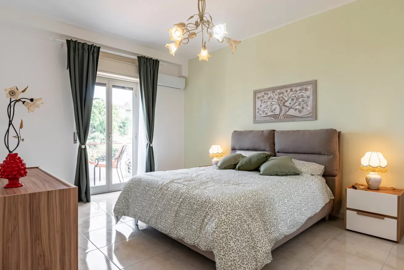 Un dormitorio con una cama bien arreglada y una puerta de vidrio que da a un balcón.