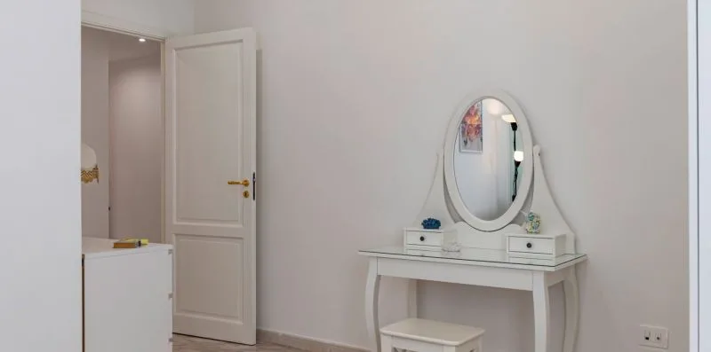 Un tocador blanco con espejo ovalado está junto a una puerta abierta.