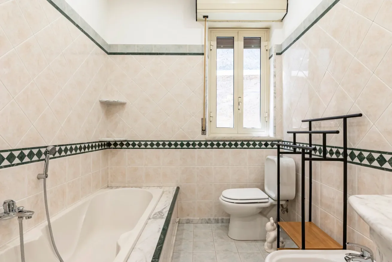 Un baño con azulejos, bañera, inodoro y ventana.