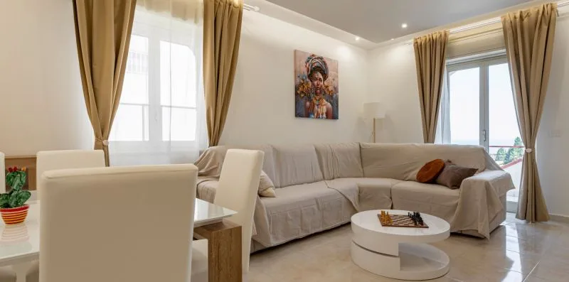 A bright living room with sectional seating, a round coffee table, and curtained windows.
