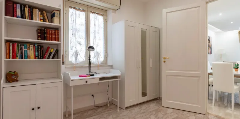 Una habitación luminosa con estanterías, un escritorio y un armario.
