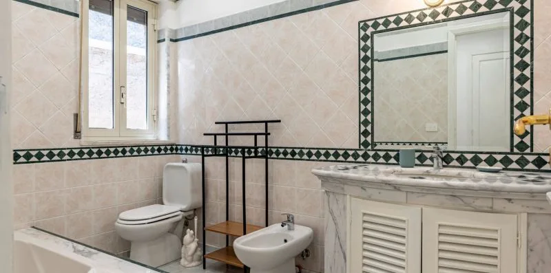 Un baño alicatado con inodoro, bidé y lavabo bajo un espejo grande.