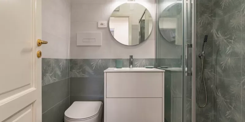 Un baño con lavabo, espejo redondo y ducha de cristal.