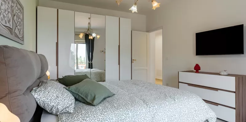 Un dormitorio con cama, armario con espejo y televisor en la pared.