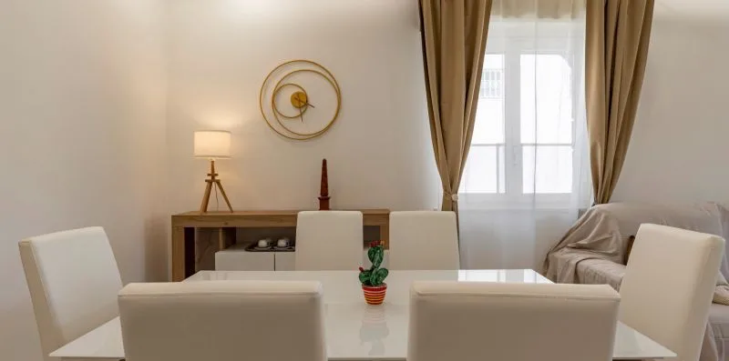 Un comedor con una mesa blanca y sillas junto a una ventana con cortinas.