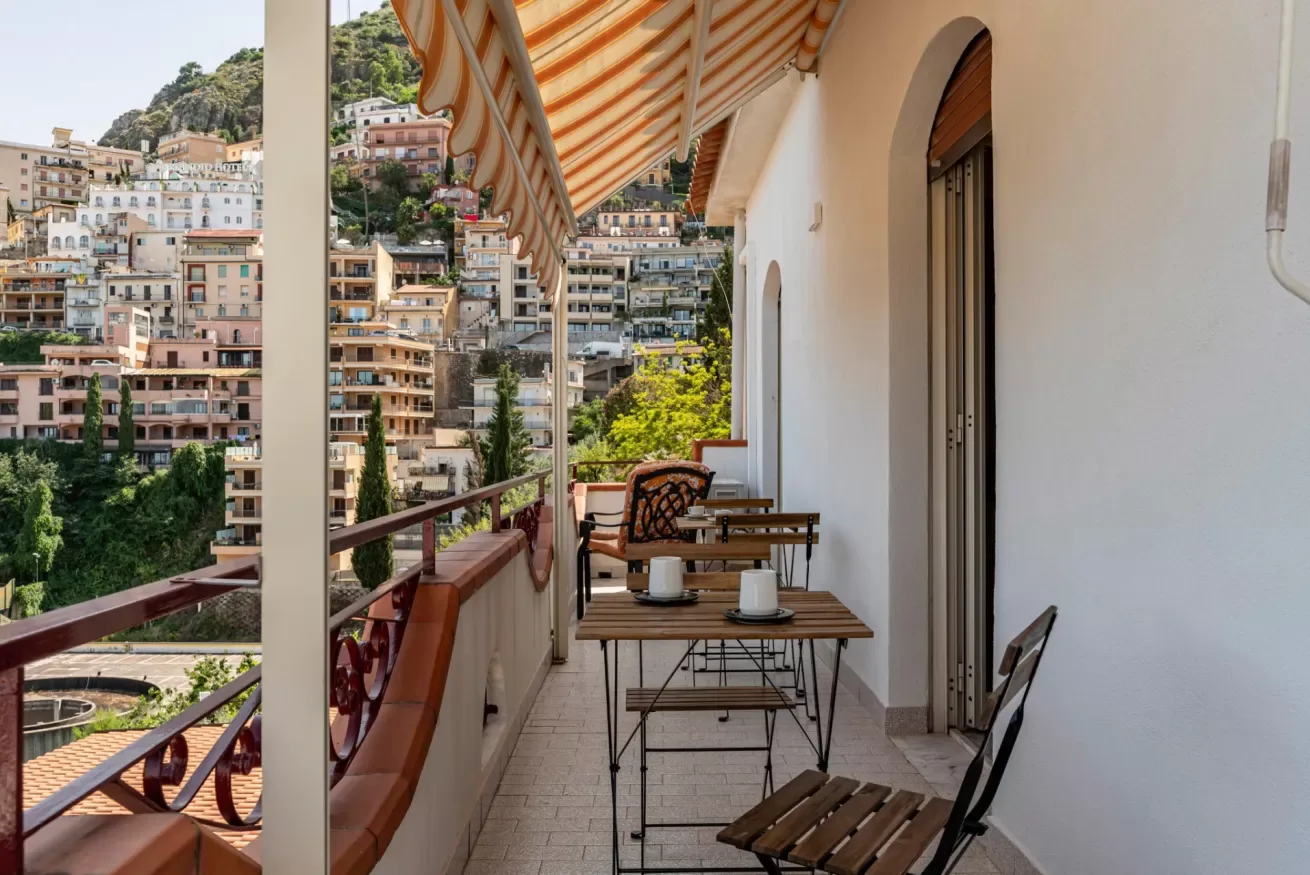 Un comedor en el balcón, con toldo a rayas, da a un barrio en la ladera.
