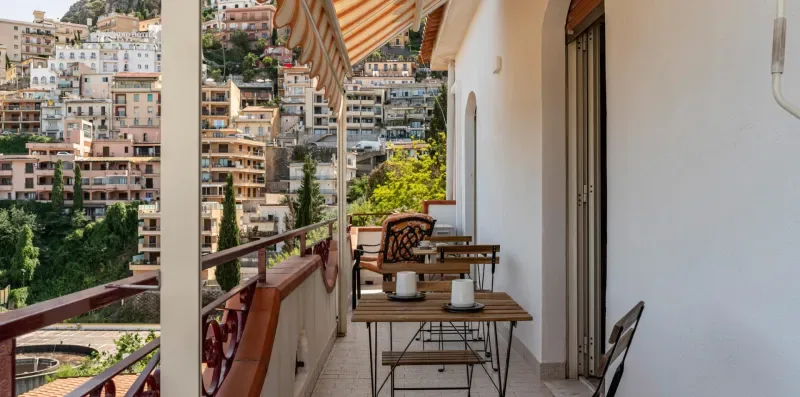 Un balcón con una pequeña mesa de comedor ofrece vistas a edificios en una ladera.