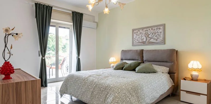 A bedroom with a neatly made bed and glass doors opening onto a balcony.