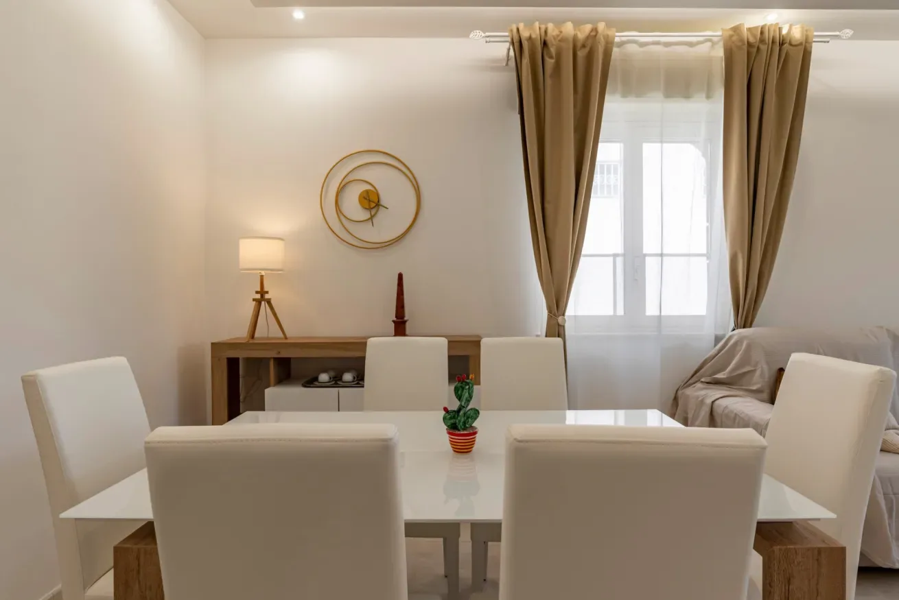 Un comedor con una mesa blanca, asientos y una ventana con cortinas.