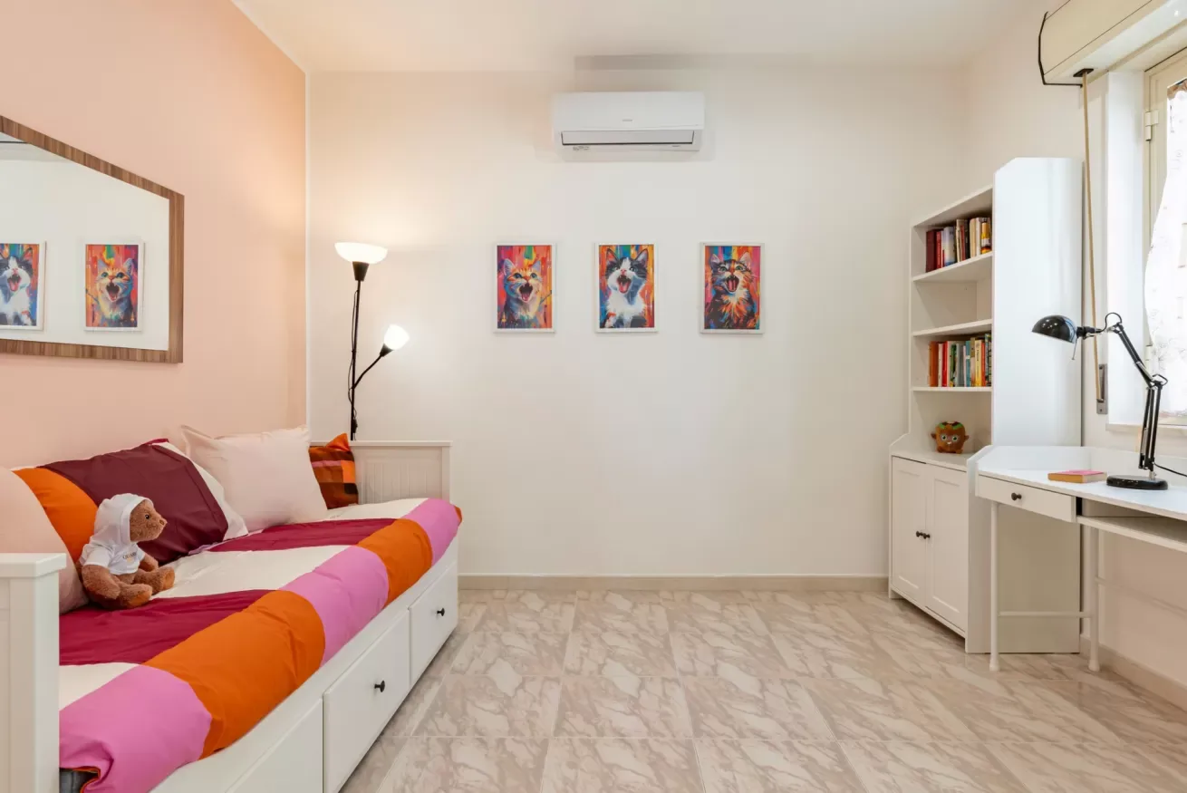 Un dormitorio con una cama colorida, cuadros y un escritorio junto a una estantería.