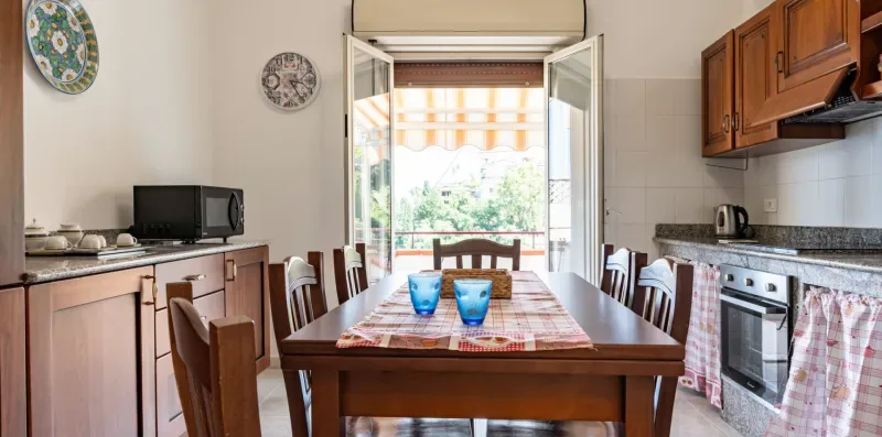 Un comedor con una mesa de madera y una ventana abierta con vistas a la vegetación.