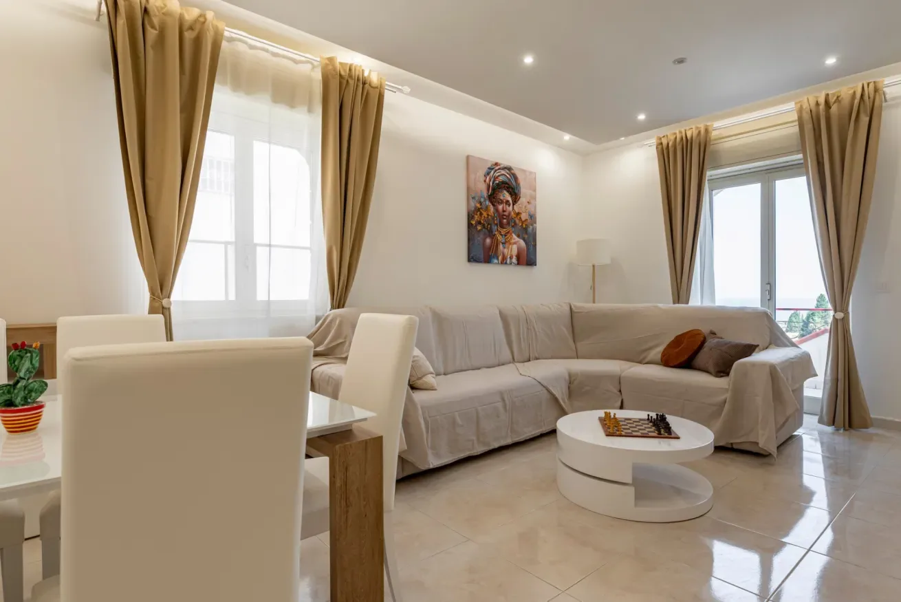 Una sala luminosa con zona de estar, mesa de comedor y grandes ventanas con cortinas.