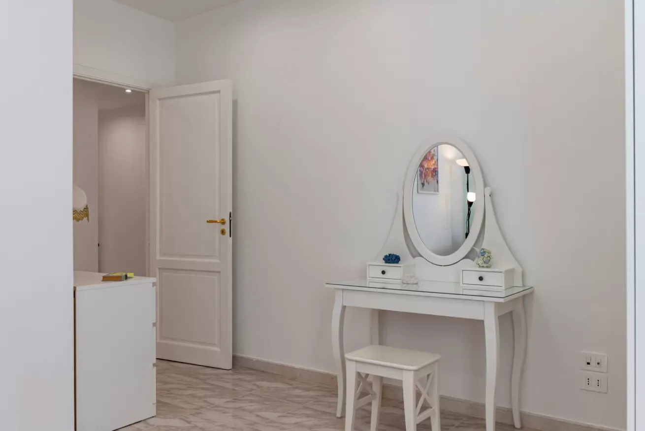 Un vestidor luminoso con un tocador blanco y un espejo ovalado.