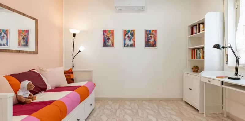 Un dormitorio con ropa de cama colorida, cuadros y un escritorio.