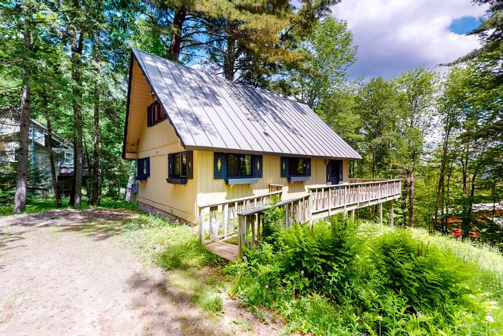 A yellow cabin sits among trees beside a raised wooden walkway.