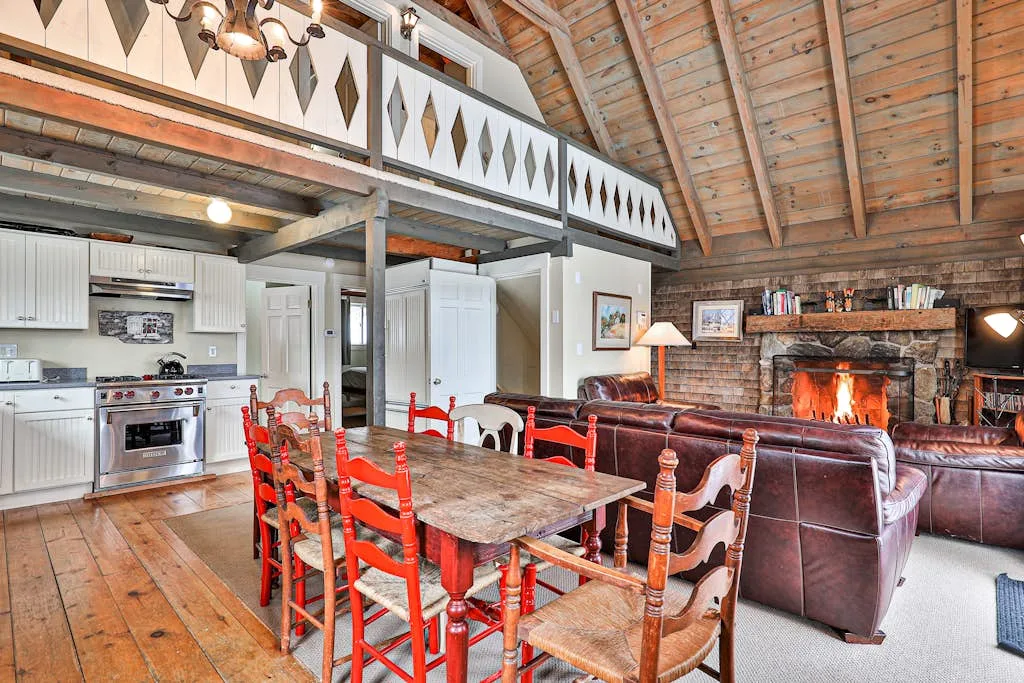 A rustic open-plan living and dining area with a kitchen, dining table, and fireplace.