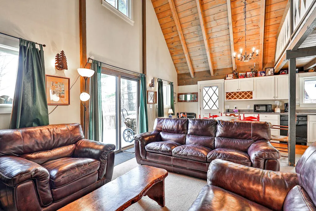 A spacious living room with leather seating, large windows, and an open kitchen.