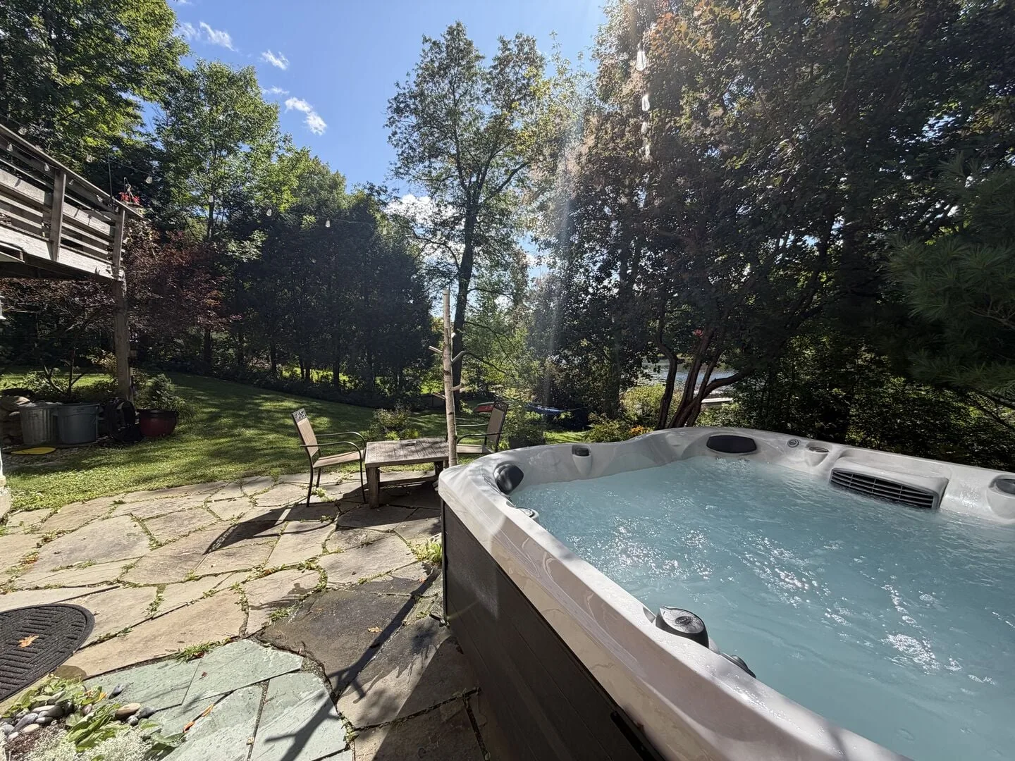 A bubbling hot tub sits on a stone patio beside a leafy garden.