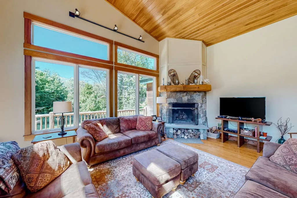 A living room with seating, a fireplace, and large windows overlooking trees.