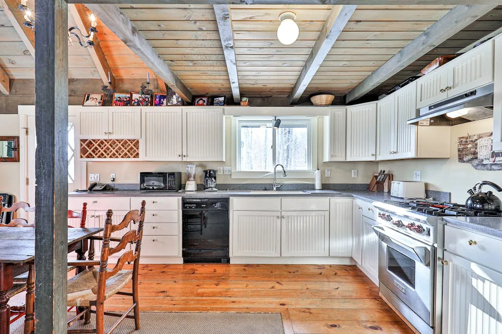 A bright kitchen with white cabinets, wood floors, and exposed ceiling beams.