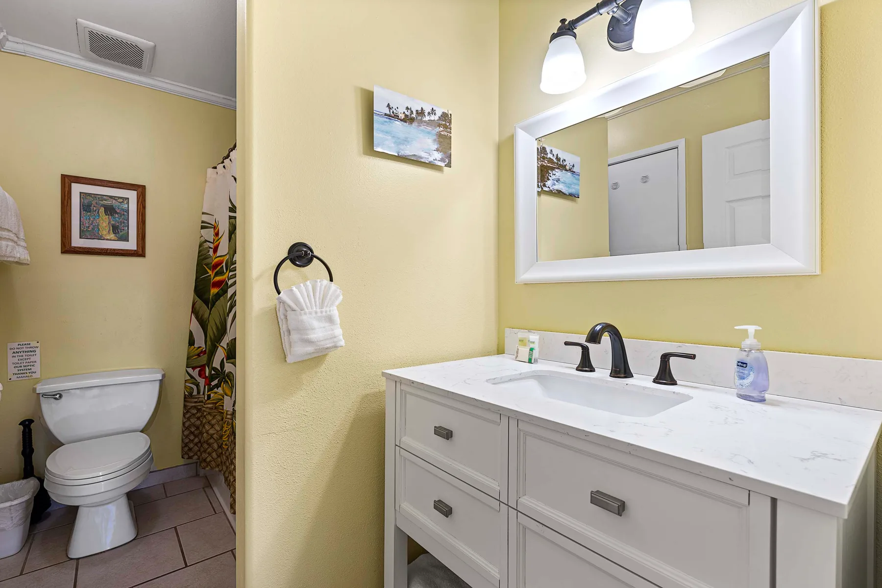 Un baño con un tocador blanco y un inodoro junto a una cortina de ducha estampada.