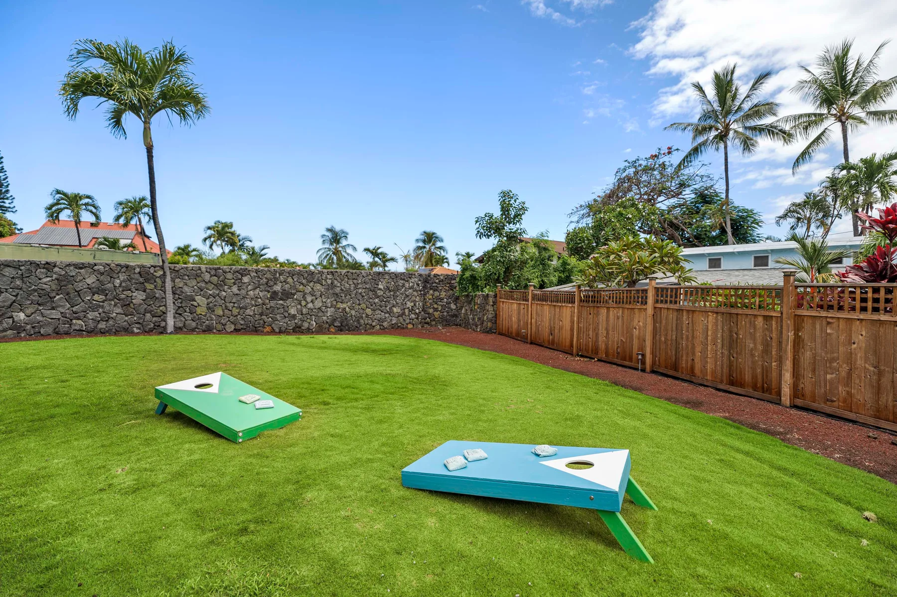 Una zona recreativa al aire libre con césped tiene dos tableros de cornhole y una cerca de madera.