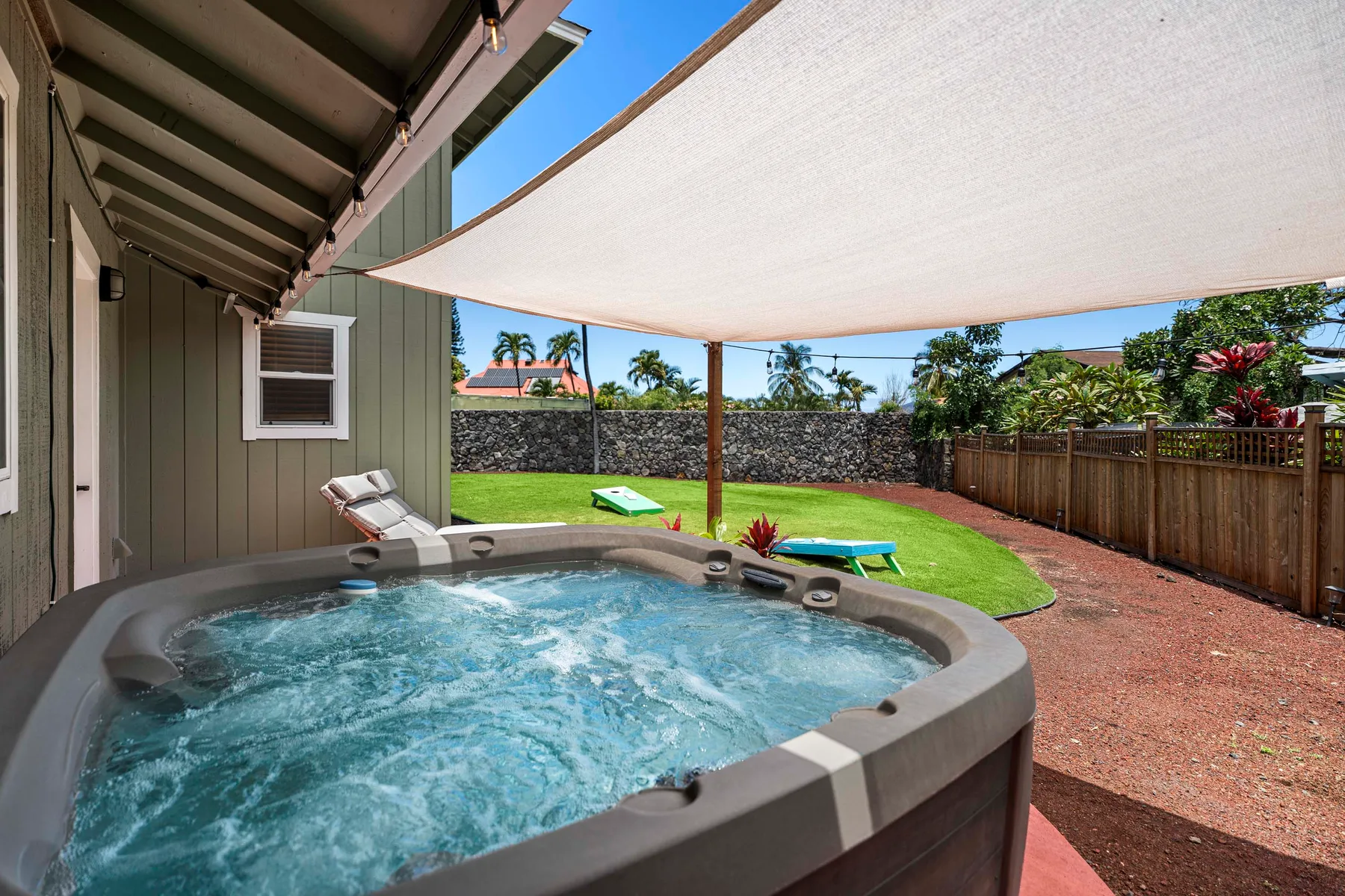 Una bañera de hidromasaje exterior está junto a un césped bajo una vela de sombra.