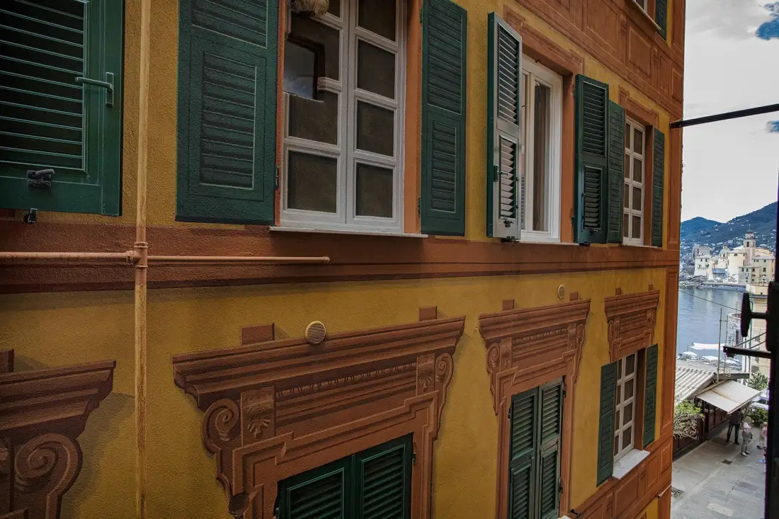 A yellow building facade with green shutters and a waterfront view.