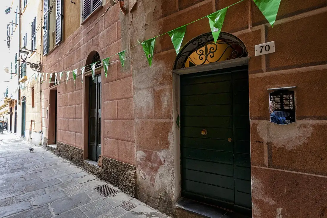 A narrow stone-paved street runs beside a building with a dark doorway and green bunting.
