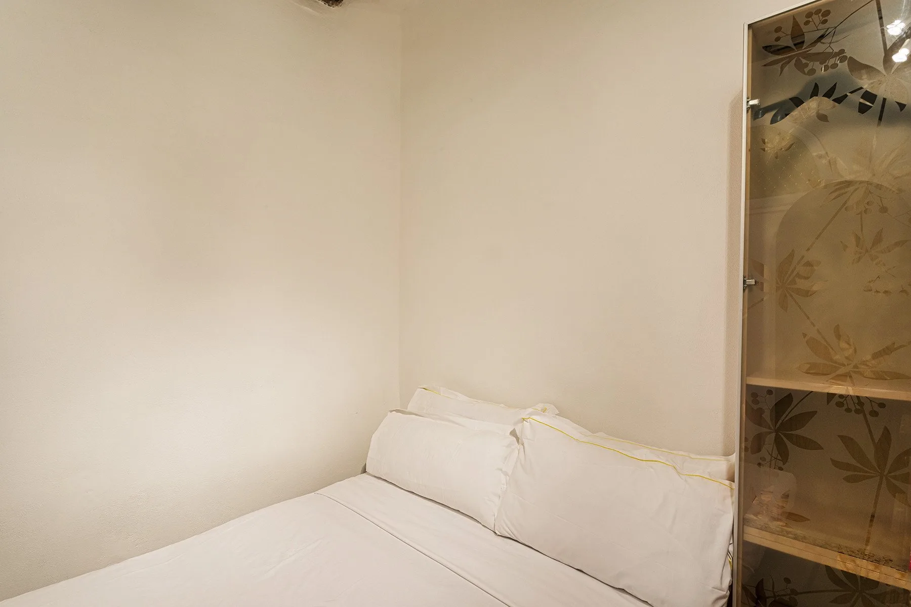 A bedroom with white bedding and a decorative patterned panel beside the bed.