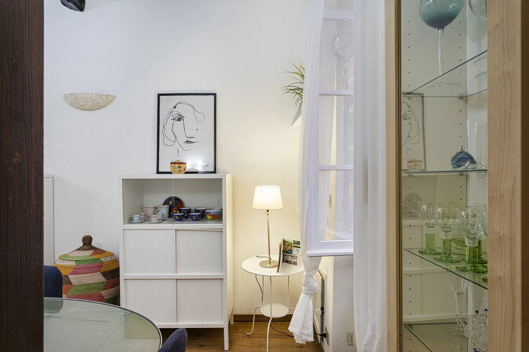A bright sitting area with a round table, lamp, and glass display cabinet.