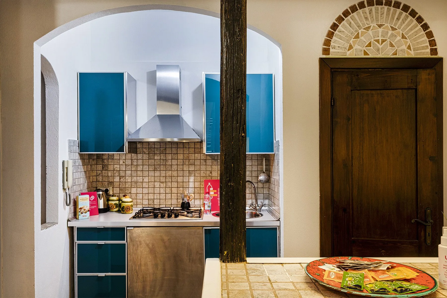 A compact kitchen with blue cabinets, a tiled backsplash, and a wooden counter.