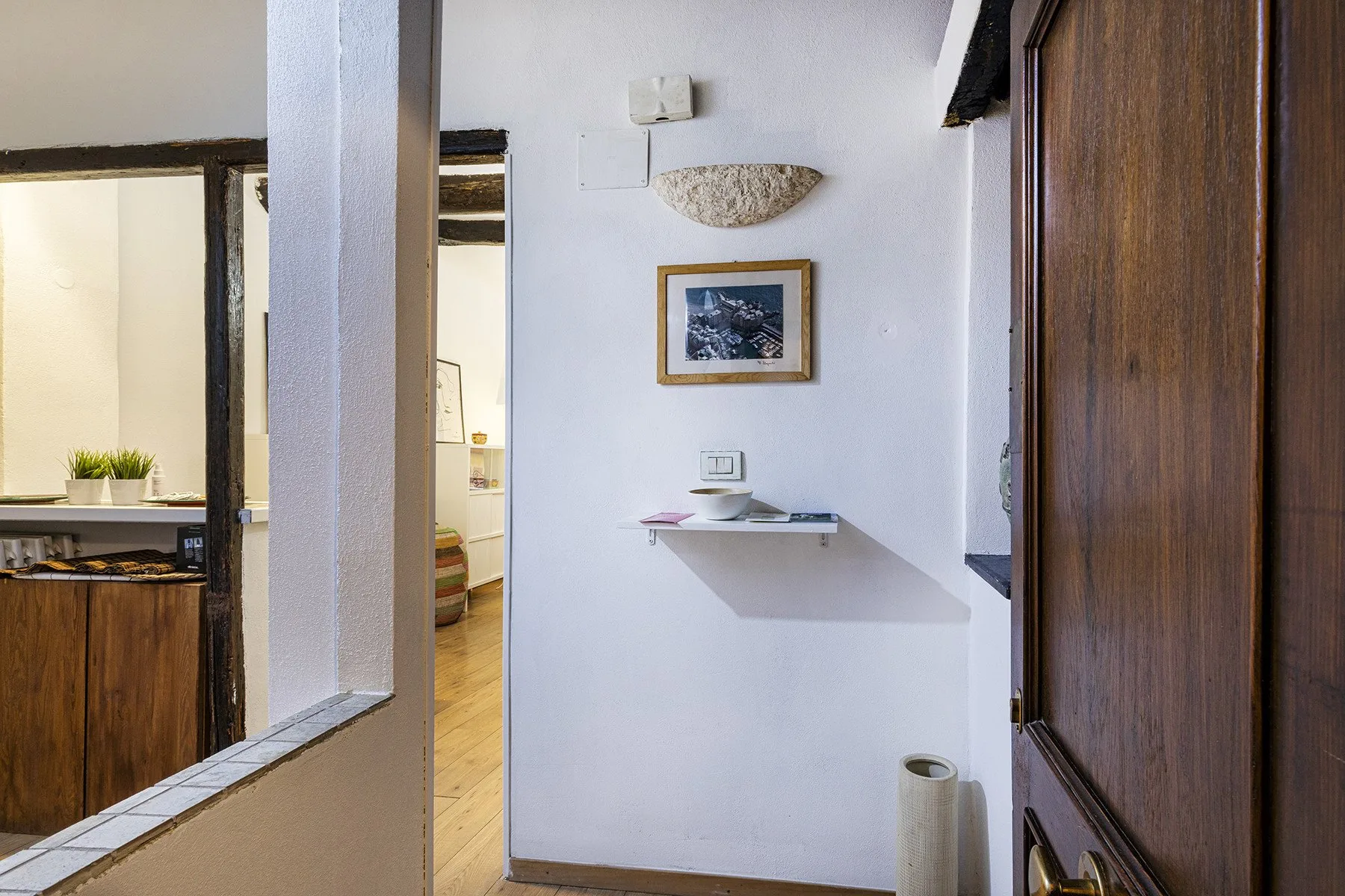 A bright interior hallway with a small wall shelf and framed artwork.