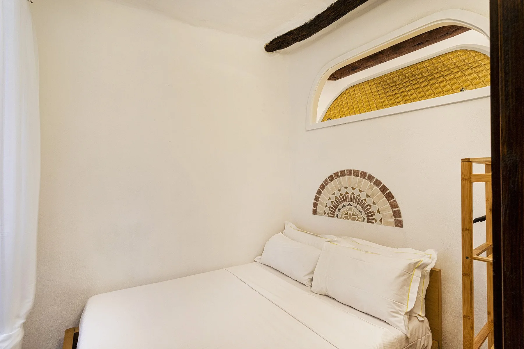 A bedroom with a white bed beneath a small arched window.