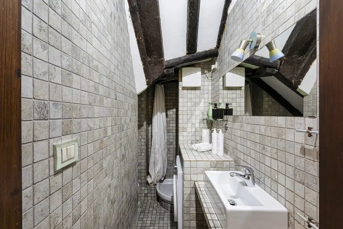A tiled bathroom with a bathtub, sink, and exposed dark ceiling beams.