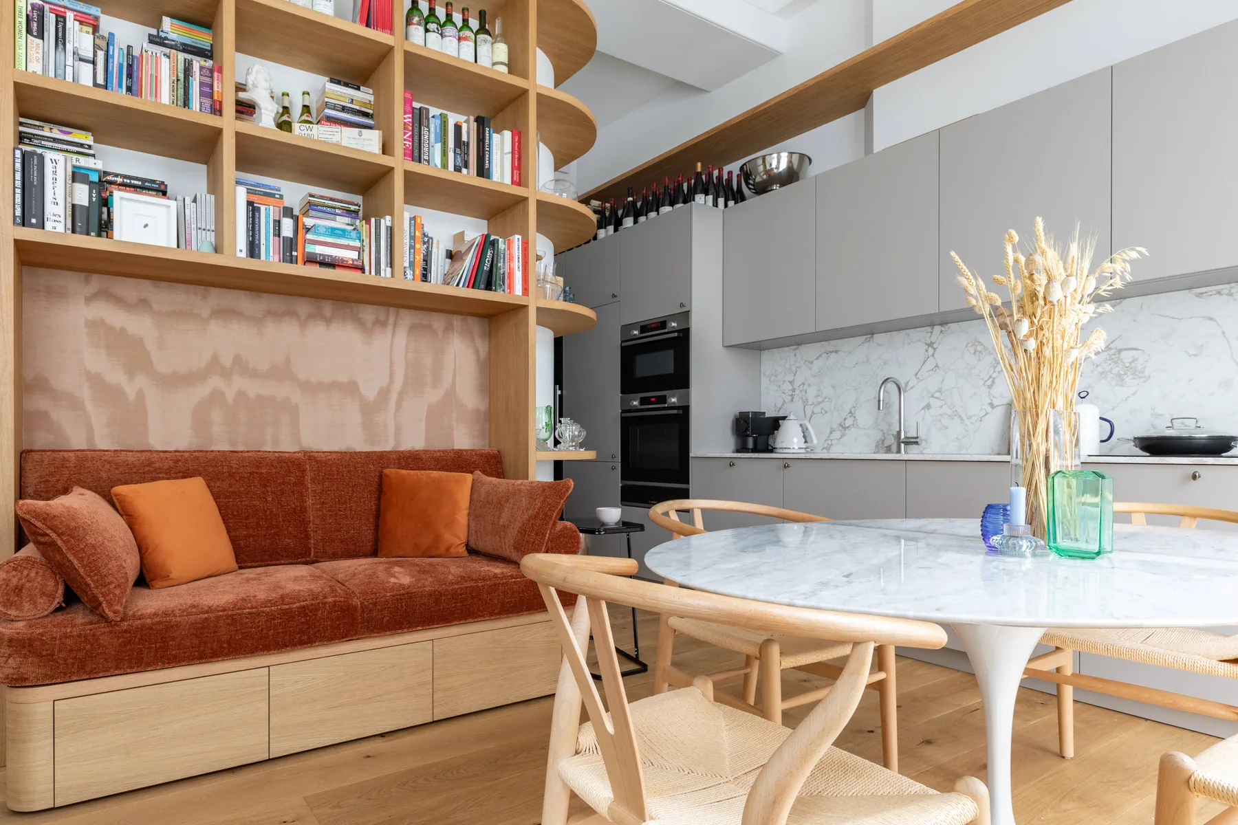 Una sala de estar con un sofá color óxido junto a una cocina abierta y una mesa de comedor.