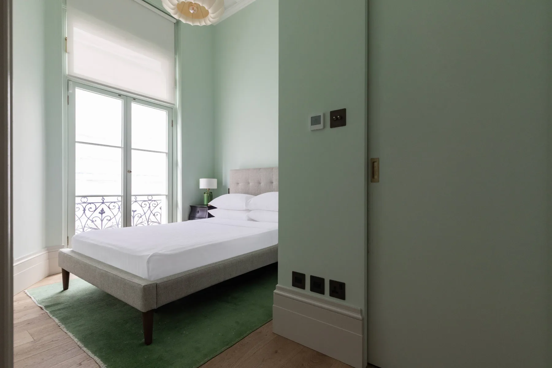 Dormitorio con una cama junto a puertas de vidrio altas y una alfombra verde.