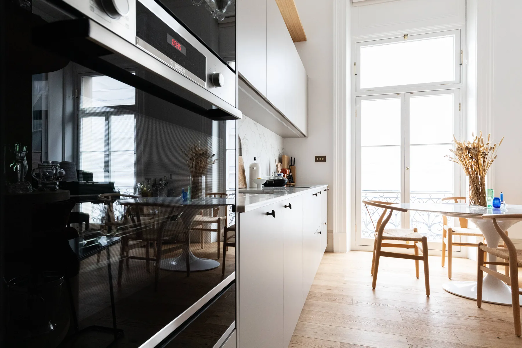 Una cocina luminosa con armarios blancos, una mesa de comedor y grandes ventanas.
