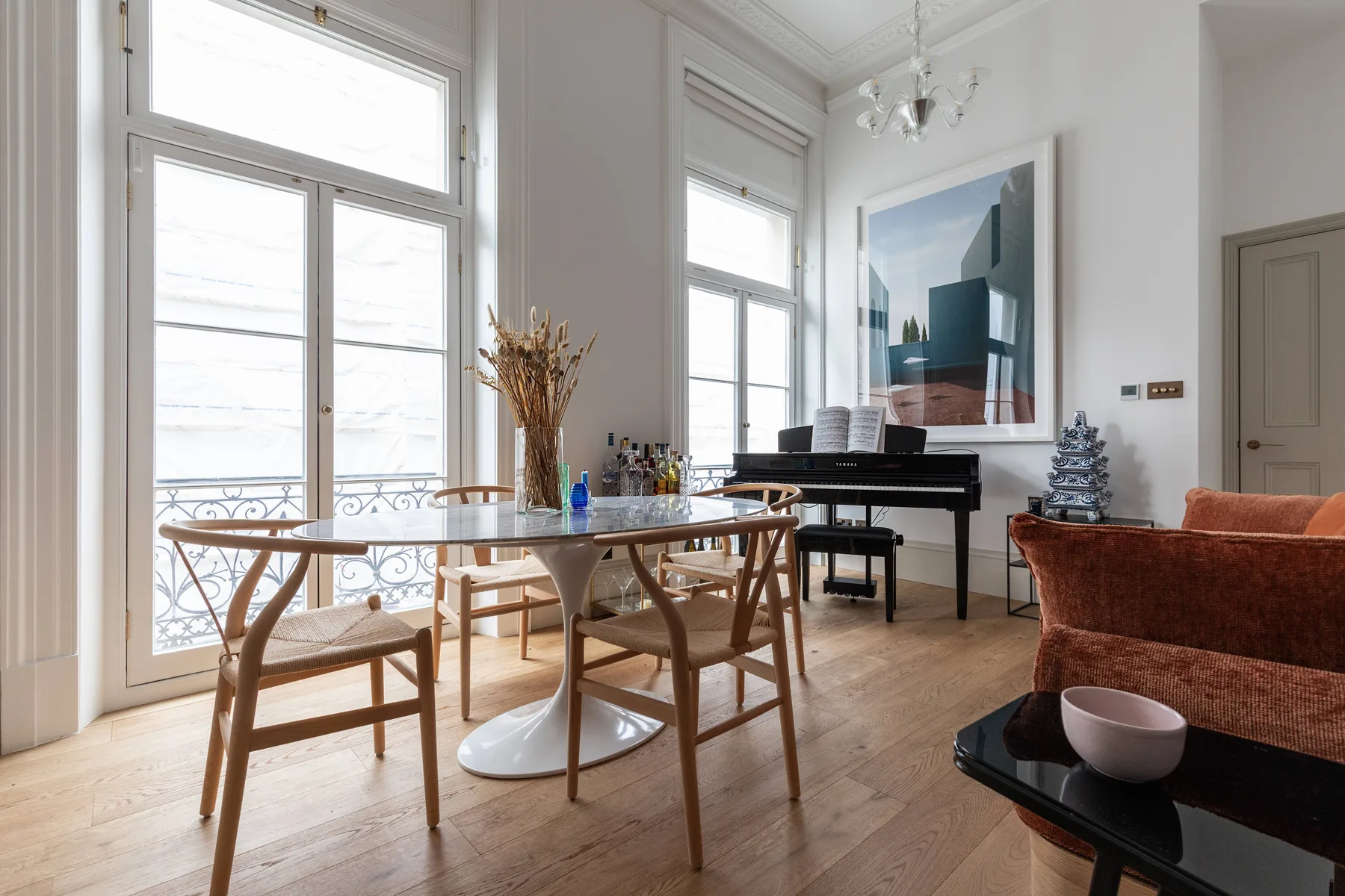 Una luminosa sala-comedor tiene una mesa, un piano y grandes ventanales.