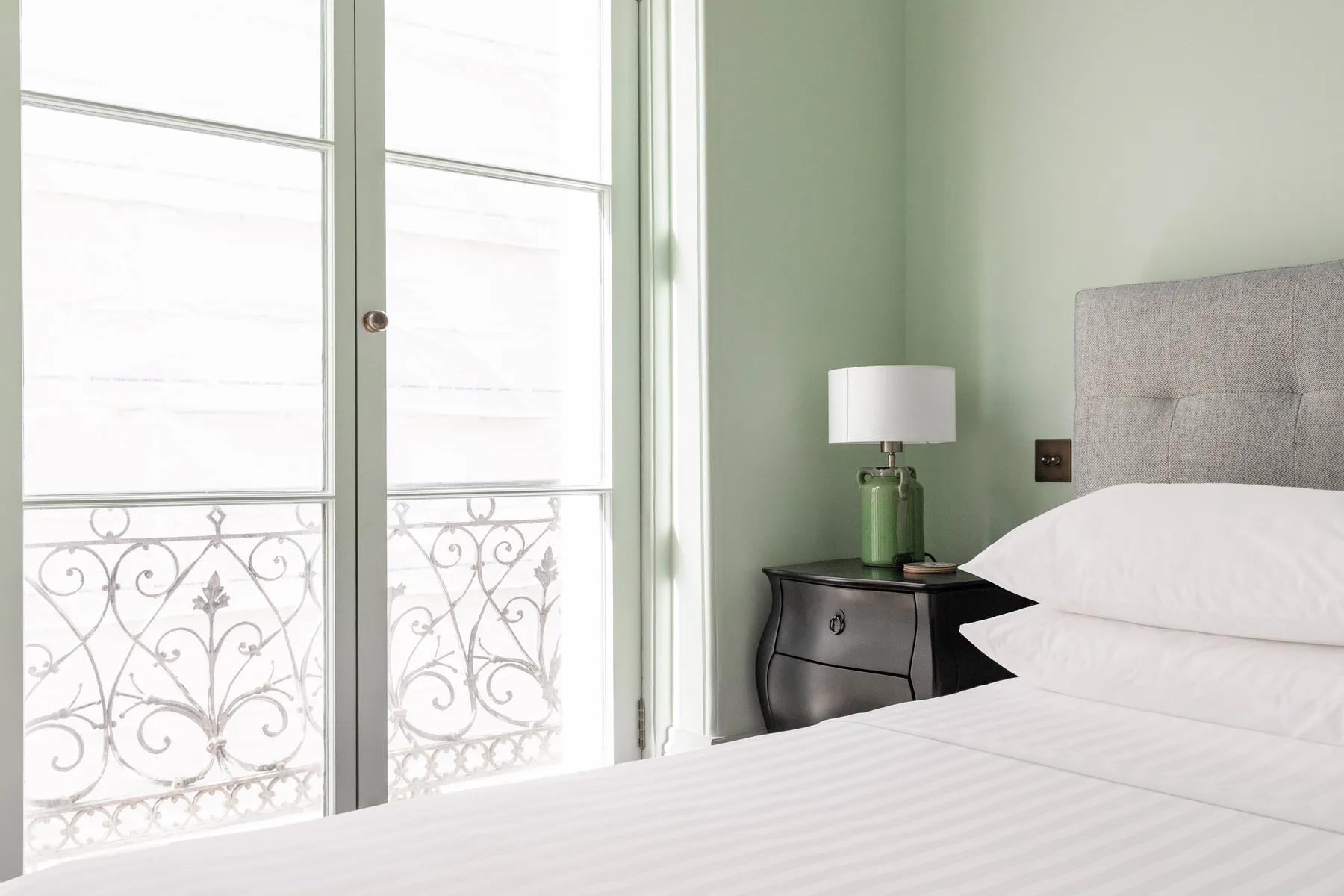 Un dormitorio luminoso con una cama tendida junto a una ventana alta.