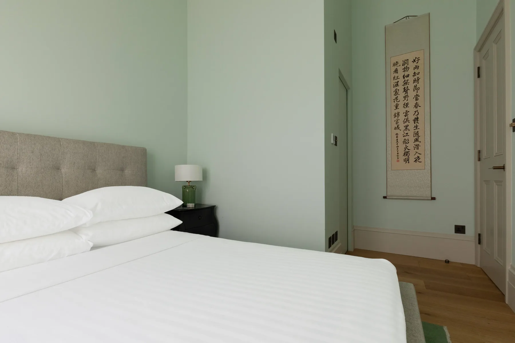 Un dormitorio con una cama bien tendida y una obra de caligrafía enmarcada.