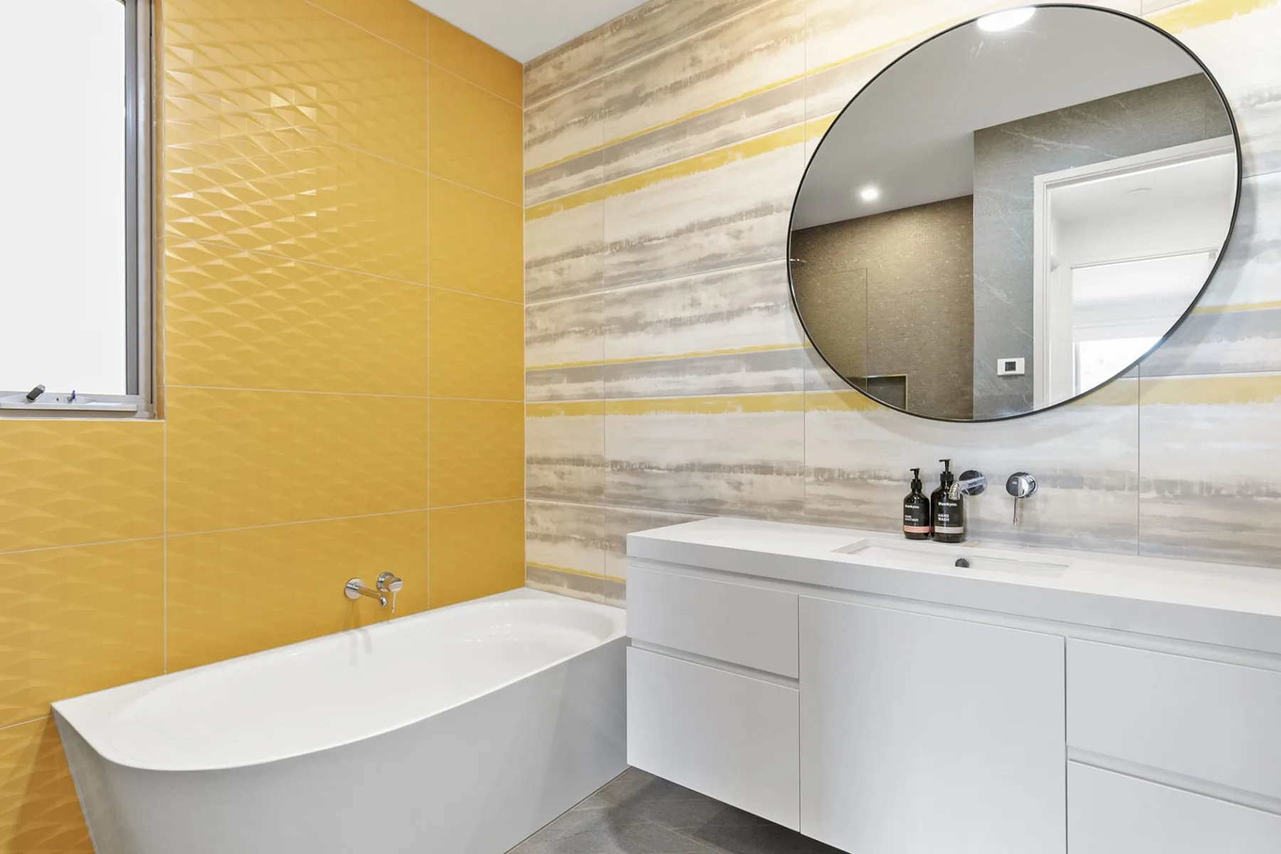 Un baño con bañera y un amplio tocador bajo un espejo redondo.