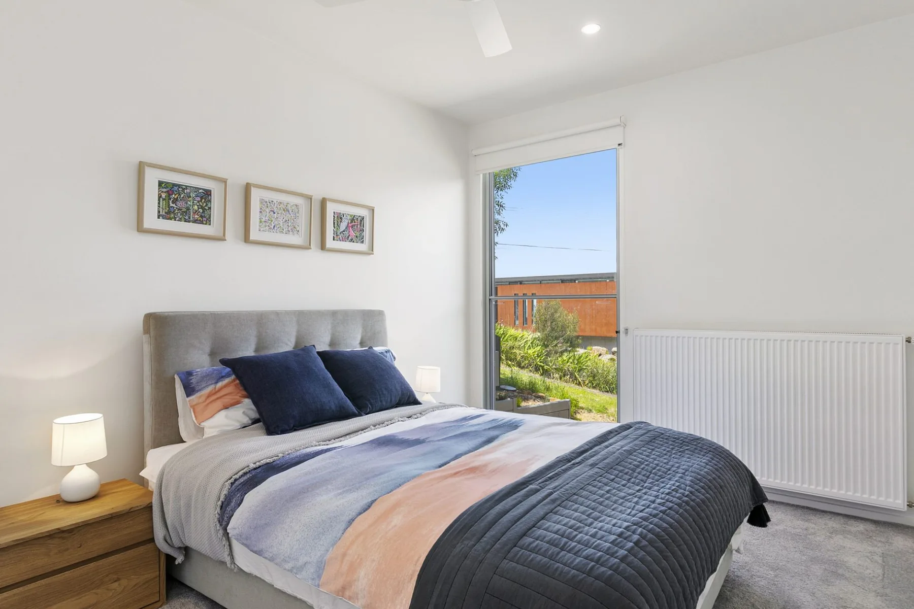 Un dormitorio luminoso con una cama, cuadros enmarcados y una ventana grande.