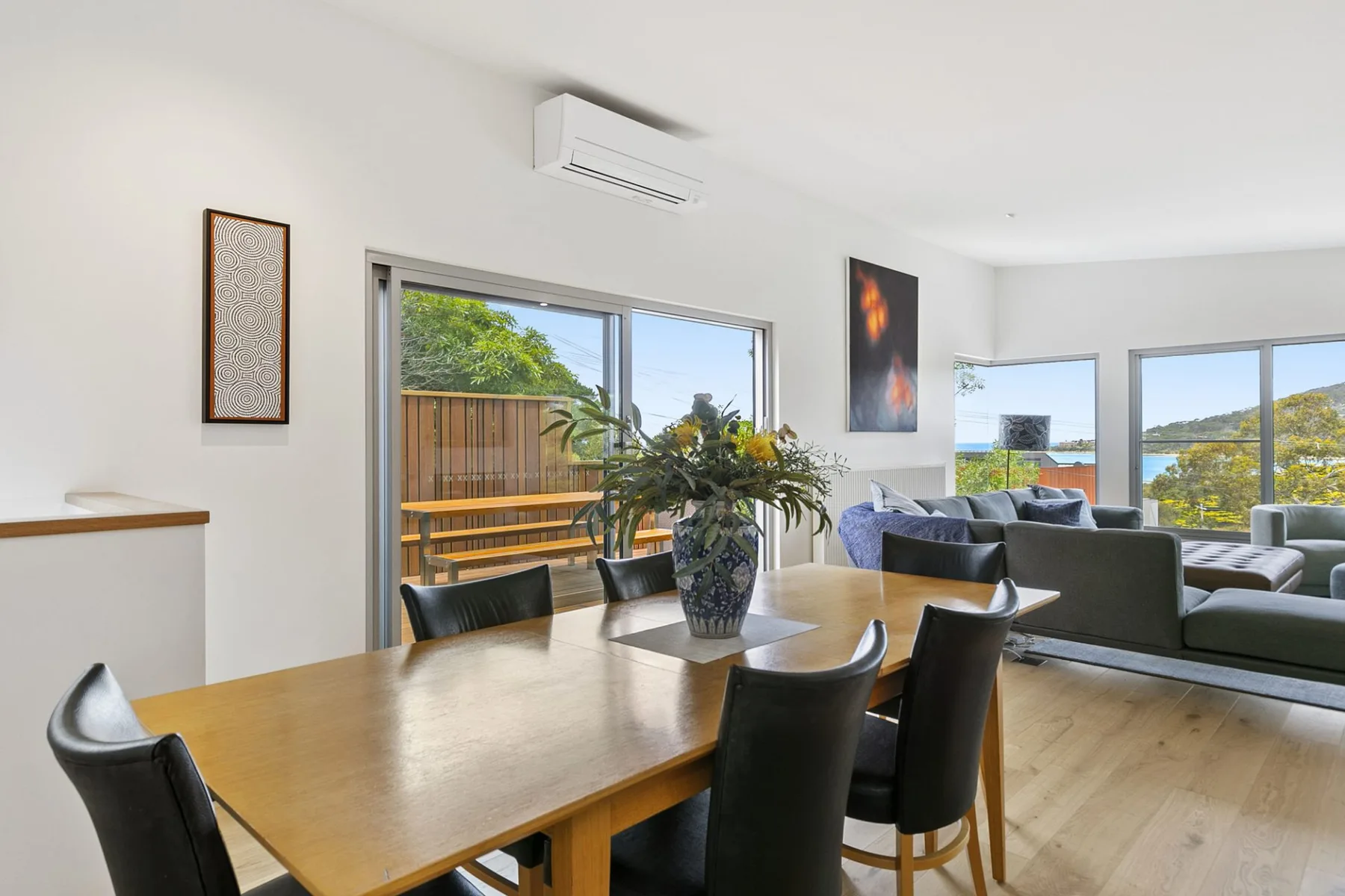 Un comedor y sala de estar con una mesa de madera y grandes ventanas.