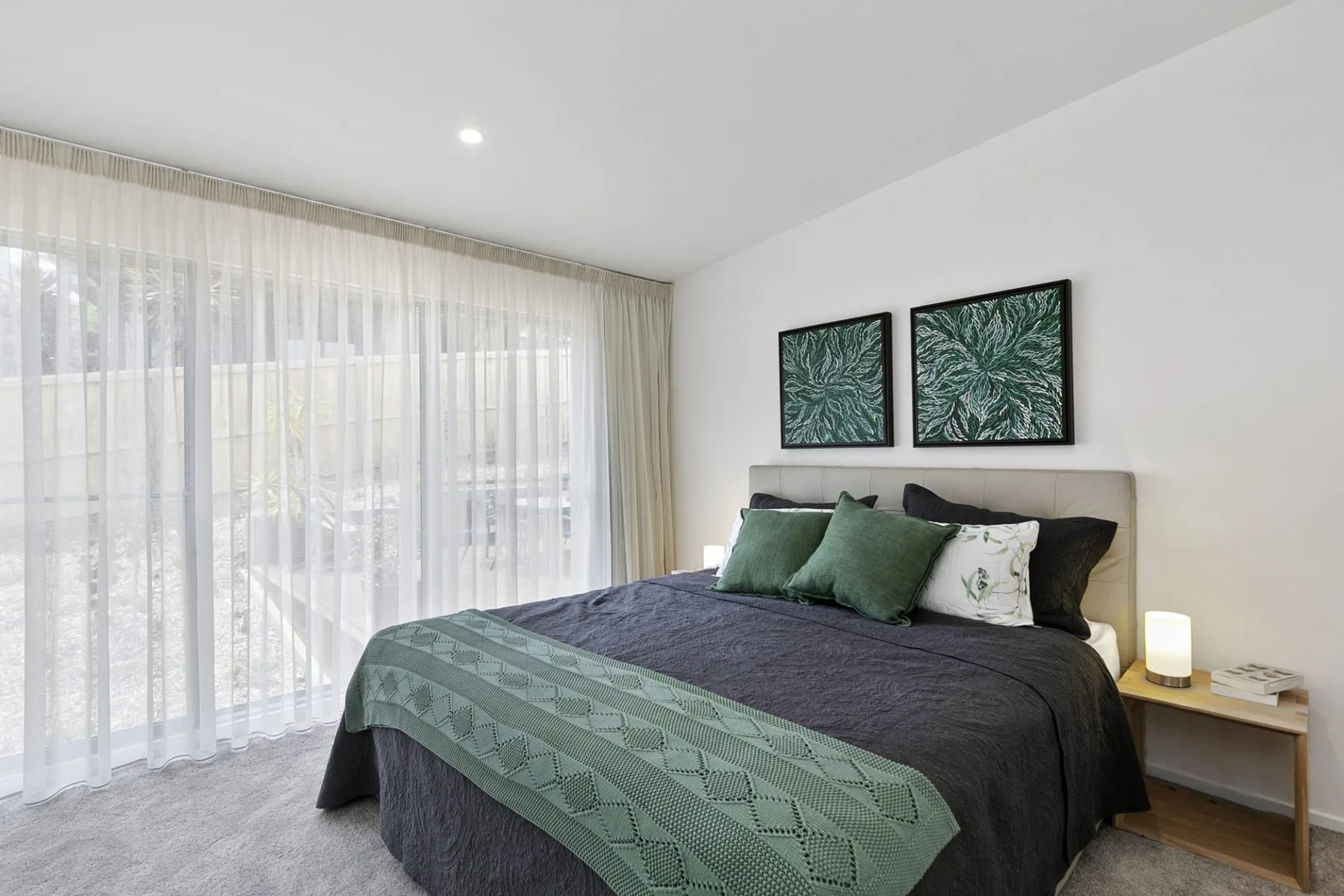 Un dormitorio luminoso con una cama tendida y cortinas translúcidas.
