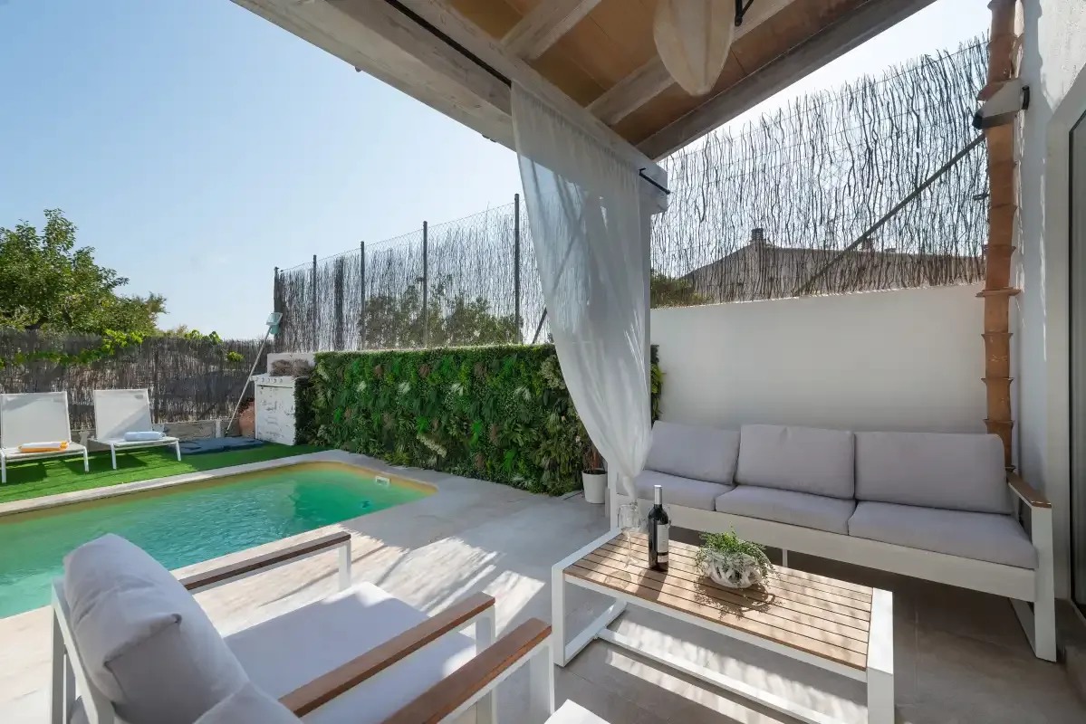 Un patio cubierto junto a una piscina, con asientos al aire libre y una mesa baja.