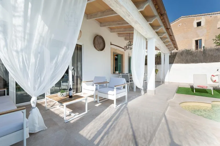 Un patio cubierto con asientos al aire libre y cortinas blancas junto a una piscina pequeña.