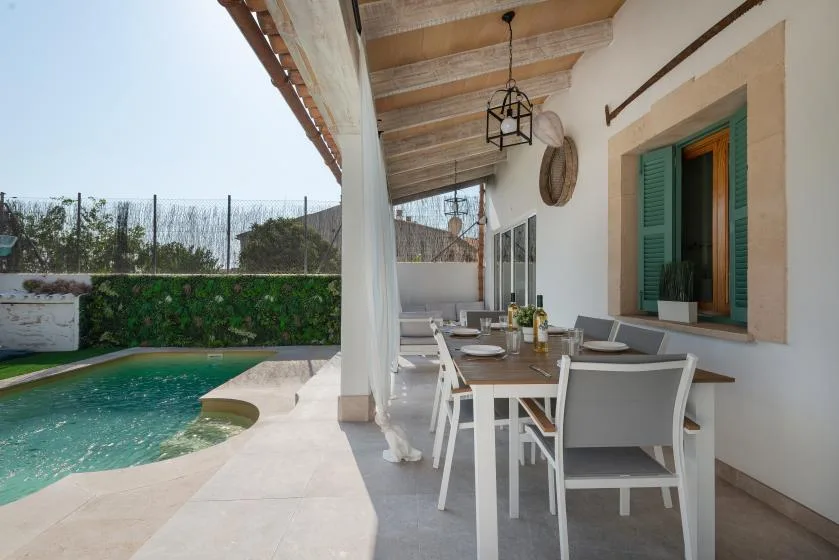 Un comedor en una terraza cubierta junto a una piscina, con una mesa larga al aire libre.