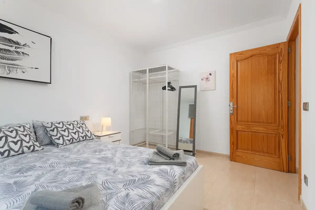 Un dormitorio con ropa de cama estampada, un espejo de cuerpo entero y una puerta de madera abierta.